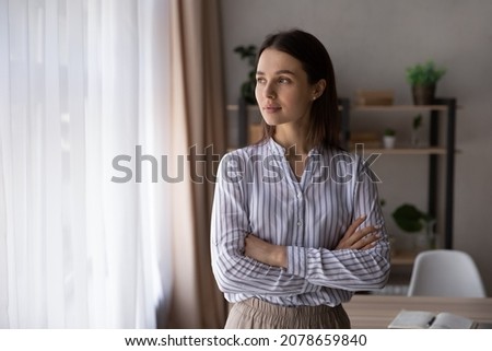 Portrait of happy dreamy young woman looking away, standing with folded arms in modern living room, visualizing future, recollecting good memories, planning weekend or thinking of problem solutions. Royalty-Free Stock Photo #2078659840