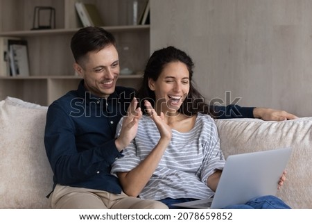 Cheery couple greeting friend start talk on videoconferencing seated on sofa with laptop. Virtual meeting with family living abroad, modern tech, videocall event activity, remote communication concept Royalty-Free Stock Photo #2078659852
