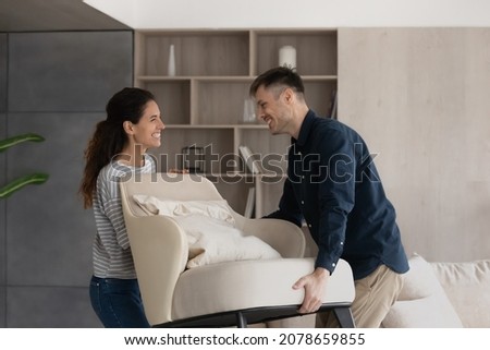 Moving day, happy buyers of fashionable furniture, bank mortgage concept. Smiling loving millennial wife and husband carry new armchair into living room, making home design improvements feel satisfied Royalty-Free Stock Photo #2078659855