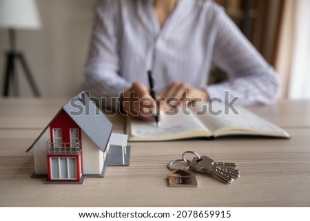 Close up young woman handwriting notes in paper organizer, sitting at table with keys and house model, household expenditures management, planning real estate investment, purchasing own accommodation. Royalty-Free Stock Photo #2078659915