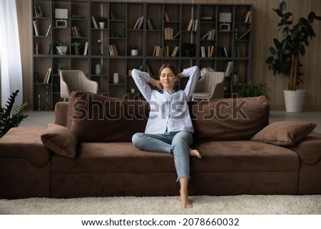 Carefree young single woman resting on comfy sofa in living room, put hands behind head close her eyes breath fresh conditioned air inside modern home. Happy flat renter, weekend relaxation concept Royalty-Free Stock Photo #2078660032