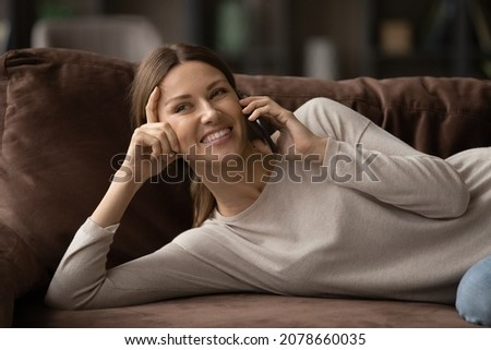 Relaxed happy beautiful woman lying on comfy sofa at home enjoy pleasant conversation on cell phone, female spend carefree weekend talking using mobile carrier operator. Leisure, connection concept Royalty-Free Stock Photo #2078660035