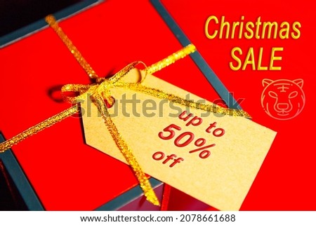 Christmas discounts in the year of the tiger. A red gift box with a golden ribbon on a red background with the text - Christmas sale and a picture of a tiger. Label on the box - up to 50 off.