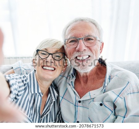 Portrait of a happy senior couple taking a selfie embracing hugging and having fun at home
