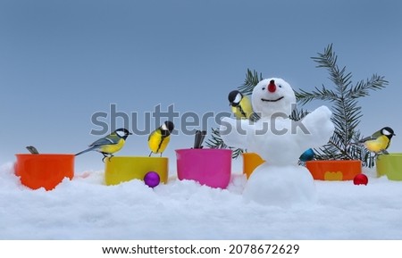 Funny tits eat from colorful bird feeders near Christmas tree with snowman. New Year and Christmas concept with copy space for holiday banner, poster, postcards, greeting, invitation, etc. 