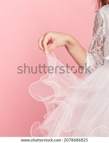 White tulle skirt on pink background. Baby white dress. Girl holds hem of skirt