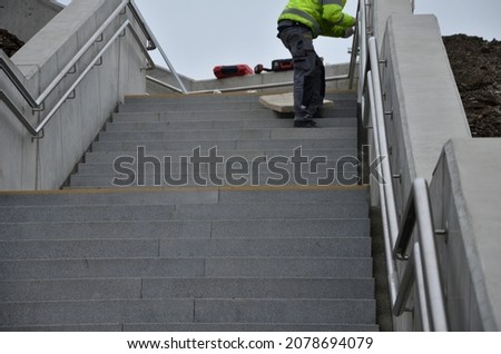 concrete staircase with massive side panels. railings are retaining walls sunk beneath the terrain. double stainless steel handle at different heights fitter worker.