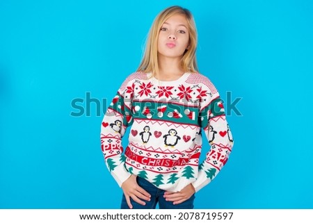 Portrait of lovely funny caucasian little kid girl wearing knitted sweater christmas over blue background sending air kiss