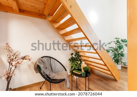 A cozy reading corner at home with a small armchair in modern design, accompanied by a similar size coffee table. It is simply located under wooden stairs and is complemented by home-grown vegetation. Royalty-Free Stock Photo #2078726044