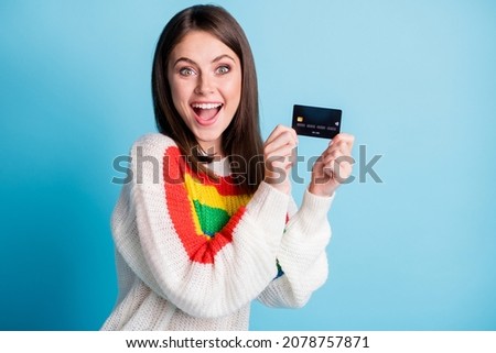 Photo of charming impressed young lady wear colorful pullover holding credit card empty space isolated blue color background
