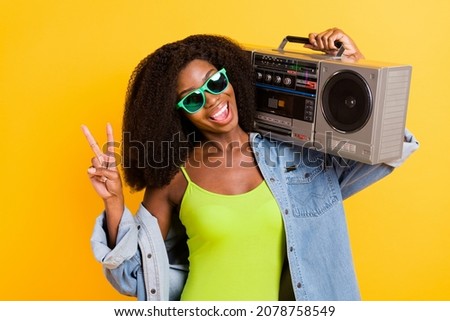 Photo of shiny cute dark skin woman wear jeans shirt listening boom box showing v-sign isolated yellow color background