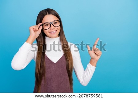 Photo of funny clever preteen girl dressed brown overall arm spectacles pointing empty space smiling isolated blue color background