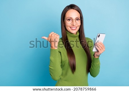 Photo of shiny sweet lady dressed turtleneck spectacles holding modern gadget pointing empty space isolated blue color background