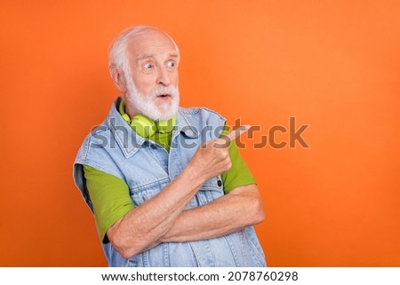 Photo of impressed shocked retired man wear jeans waistcoat headphones pointing looking empty space isolated orange color background