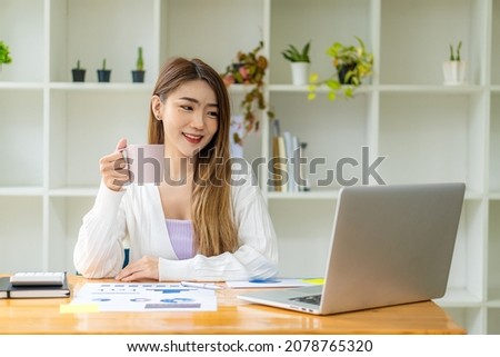 Asian businesswoman working with marketing graphs and laptop in online working concept with financial documents and analytical calculator while sitting in the office.
