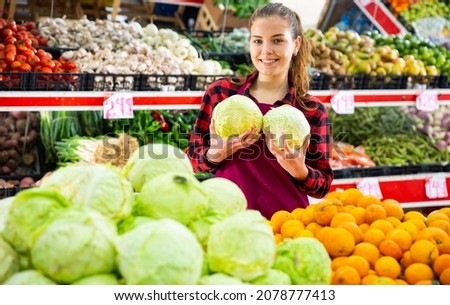 Portrait of a smiling girl of the seller near the counter, holding a cabbage in her hands