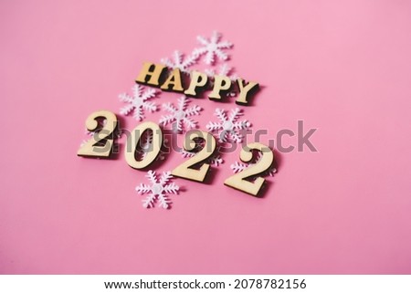 Happy New Year 2022. Quote made from wooden letters and numbers 2022 on pink background decorated snowflakes