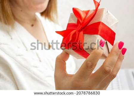 A woman's hand holds a gift box with a red bow and a laptop in her hands. The concept of online shopping for holiday gifts. Give gifts online via the Internet