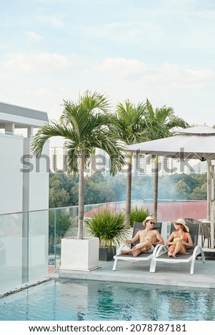 Young couple spending honeymoon at swimming pool on rooftop of hotel building