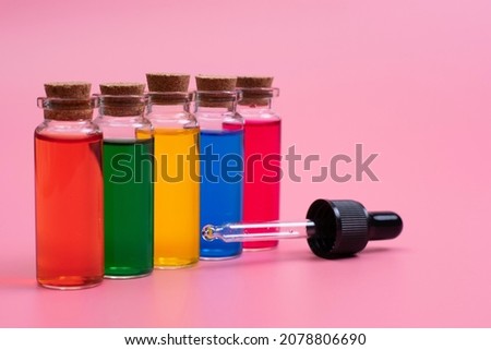 
Multi-colored liquids poured into bottles, a pipette and a dispenser are nearby. Pink background