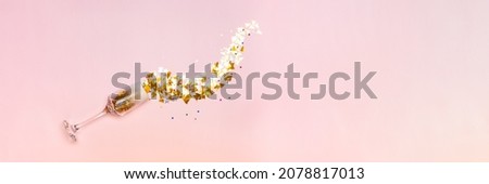 New Year card. Glass of champagne, gold sparkles in the form of trees and stars, pouring out of the glass on a pink background. Top view banner.