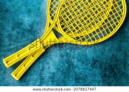 two plastic tennis rackets of light yellow color on a worn turquoise background; a children's version of the badminton tournament