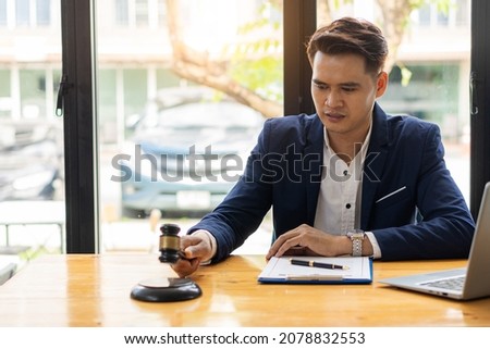Asian male lawyer working on legal contract documents in a courtroom of justice. and legal concepts In the office with hammers and scales on the table