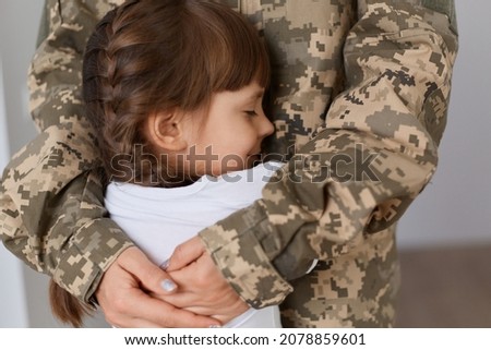 Portrait of unknown soldier woman wearing camouflage uniform comes back home after army and meeting her daughter, mother hugging her lovely charming child.