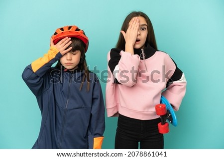 Little sisters practicing cycling and skater isolated on blue background with surprise and shocked facial expression