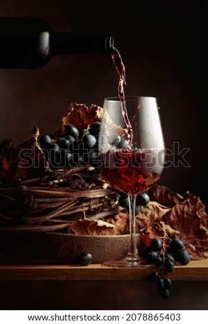 Wine is poured into a glass. Red wine and bunch of grapes on vintage wooden table.