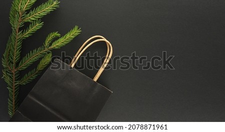 Fir branch and black paper shopping bag on black background with copy space for text, flat lay top view template. Black Friday sale, shopping concept