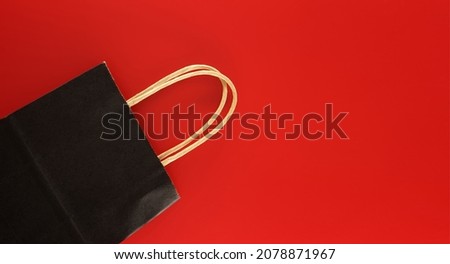 Black paper shopping bag on red background with copy space for text. Black Friday sale, shopping concept