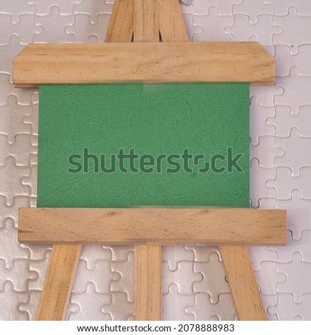 A green board on wooden easel with white puzzle board as background. Copy space for add-on.