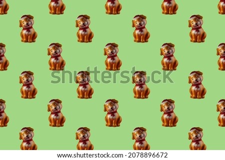 A toy dog in a red hat and with a scarf tied in the form of a seamless pattern on a green background. Christmas Seamless Pattern.