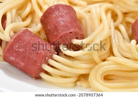 Close-up image of uncooked spaghetti that are used to skewer sliced hot dog   