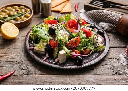Plate with tasty Greek salad and ingredients on wooden background