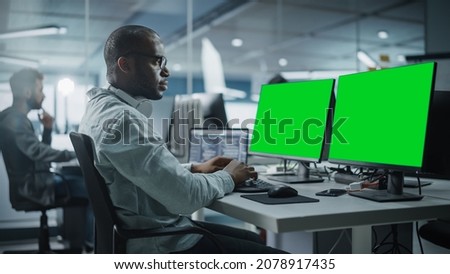 Multi-Ethnic Office: Black IT Programmer Working on Computer with Green Screen Chroma Key Display. Male Software Engineer Developing App, Program, Video Game. Terminal with Code Language.