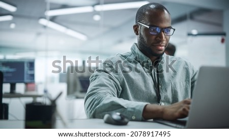 Modern Office: Portrait of Motivated Black IT Programmer Working on Laptop Computer. Male Specialist Create Website, Software Engineer Develop App, Program, Video Game. Stress Free Inclusive Space Royalty-Free Stock Photo #2078917495