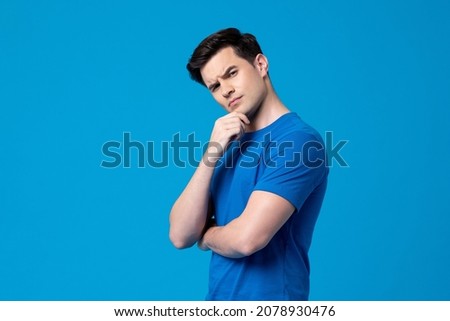 Young curious handsome Caucasian man thinking with hand touching chin in  isolated studio blue background Royalty-Free Stock Photo #2078930476