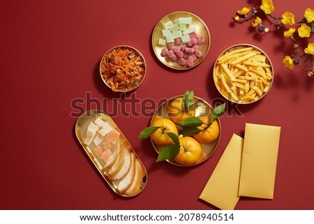 Chinese new year holiday with mandarin orange candy jam , fried potato , flower and red pocket biscuit in golden dish , photography Tet holiday content , top view