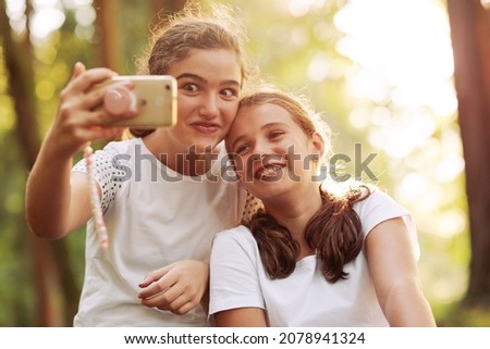 Cute young girls posing together in the forest, they are taking selfies with a smartphone