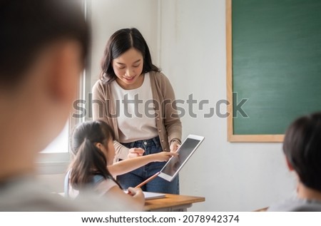 Asian Beautiful female teacher teaching Asian girl learning with digital tablet in classroom at primary school. Royalty-Free Stock Photo #2078942374