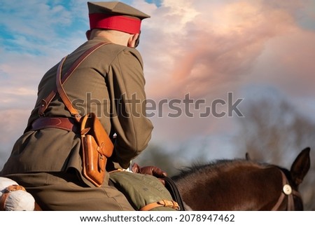 Soldier on horseback in rear view against a sky with apricot colored clouds. Royalty-Free Stock Photo #2078947462