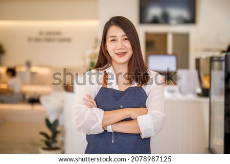 Portrait of a happy young asian business owner at small entrance looking at camera near a counter in her cafe.