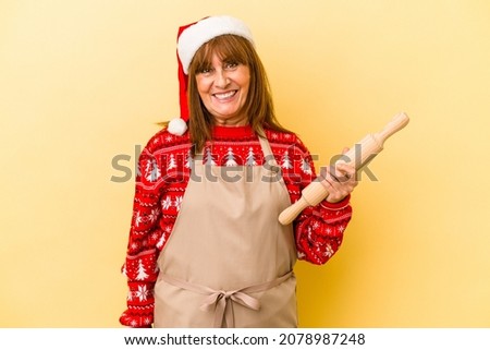 Middle age caucasian woman cooking cookies for christmas isolated on yellow background happy, smiling and cheerful.