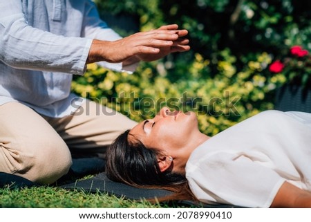 Woman in Reiki spiritual healing session. Reiki therapist holding hands above heart chakra and transferring energy. Peaceful woman is lying with her eyes closed. Royalty-Free Stock Photo #2078990410