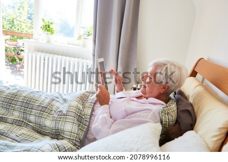 Sick elderly woman in bed in a retirement home or at home with video chat on the tablet computer