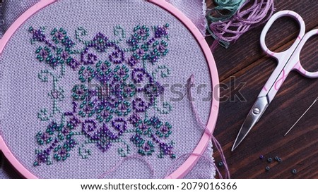 the process of cross stitch with beads in a pink hoop and accessories on a wooden table	