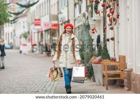 Street style portrait of young beautiful fashion woman walking in European city on winter holidays, holding Christmas bags. Stylish model in casual clothes with long hair.