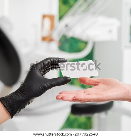 Close up of female stomatologist hand in black sterile gloves giving clinic business card to patient. Doctor handing young woman visiting card. Concept of dentistry, dental care and stomatology.